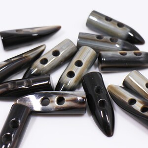 May include: A group of black and brown horn buttons with two holes each. The buttons are shaped like a pointed oval and have a glossy finish.