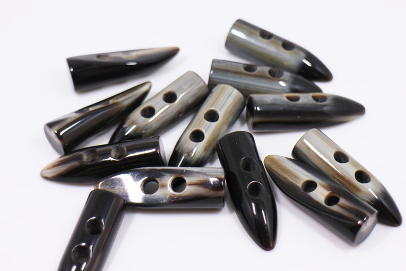 May include: A group of black and brown horn buttons with two holes each. The buttons are shaped like a pointed oval and have a glossy finish.