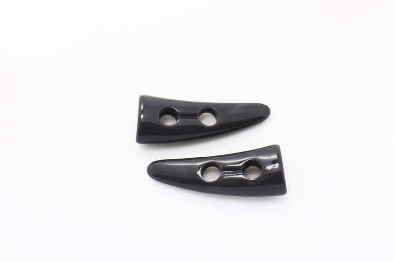 May include: Two black plastic horn-shaped toggles with two holes each.
