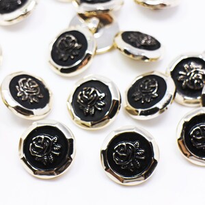 May include: A collection of black and gold buttons with a raised rose design. The buttons are round and have a slightly textured surface.
