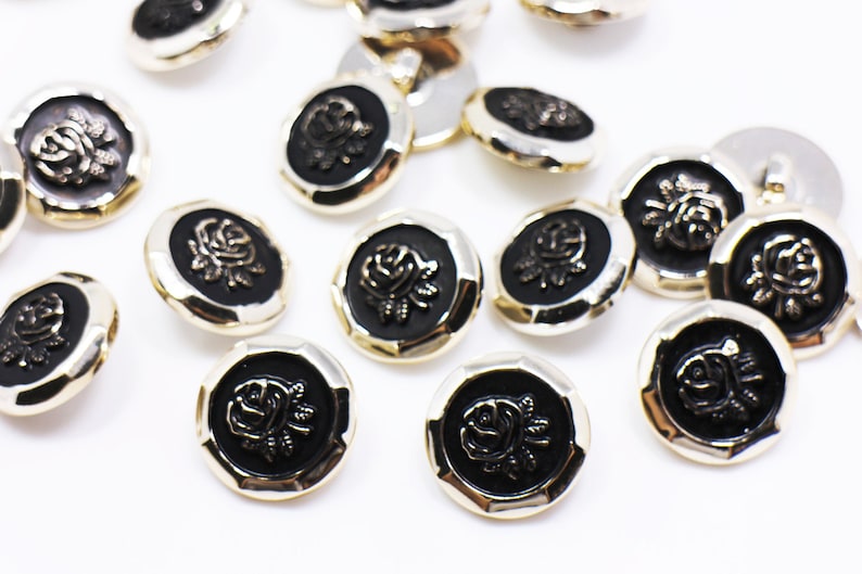 May include: A collection of black and gold buttons with a raised rose design. The buttons are round and have a slightly textured surface.