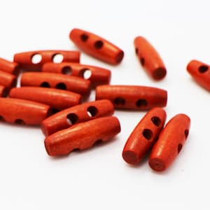 May include: A group of 14 wooden toggle buttons in a reddish-brown colour. The buttons are oval shaped with two holes each.