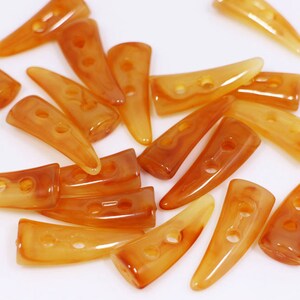 May include: A group of 18 amber-colored plastic buttons shaped like horns with two holes each. The buttons are scattered on a white surface.