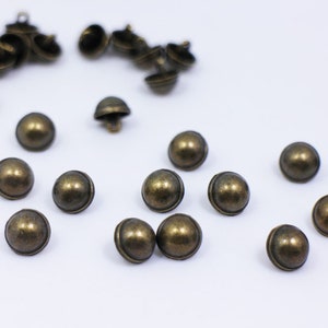Peut inclure: Un ensemble de boutons en métal de forme bombée de couleur or antique. Les boutons sont éparpillés sur une surface blanche.