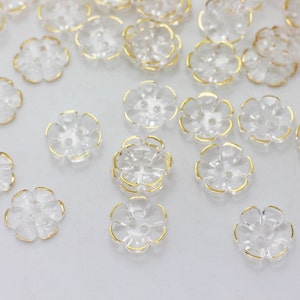 May include: A collection of clear plastic flower-shaped buttons with gold trim.