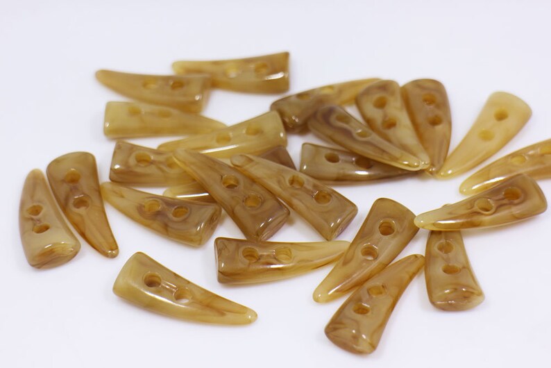 May include: A group of 20 brown plastic buttons with two holes each. The buttons are shaped like a pointed horn and have a marbled pattern.