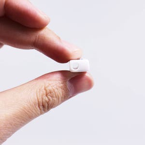 May include: A white pill held between two fingers.