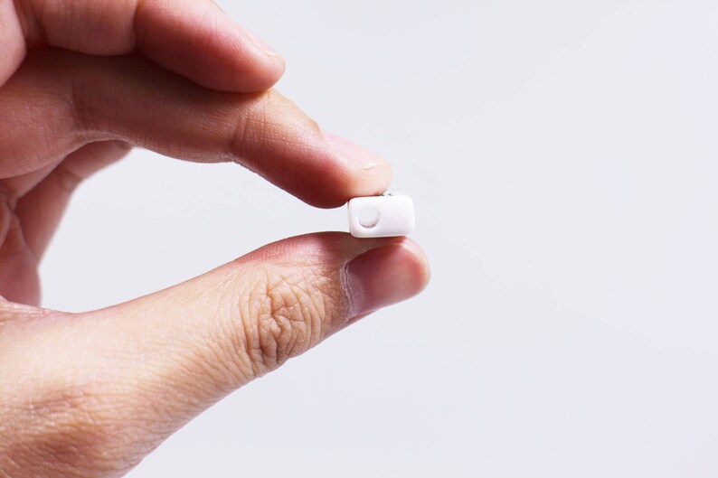 May include: A white pill held between two fingers.