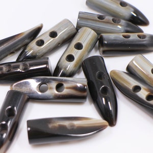 May include: A collection of brown and black horn toggle buttons with two holes each. The buttons are in various shapes and sizes, with some being pointed and others being rounded.