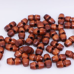 May include: A pile of brown wooden toggle buttons. The buttons are approximately 2.5 cm long and have a hole in the centre.