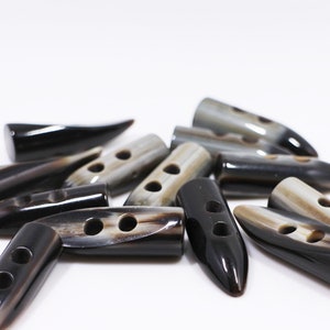 May include: A group of black and white horn toggle buttons with two holes each. The buttons are shaped like a pointed oval and have a glossy finish.