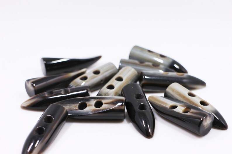 May include: A group of black and white horn toggle buttons with two holes each. The buttons are shaped like a pointed oval and have a glossy finish.