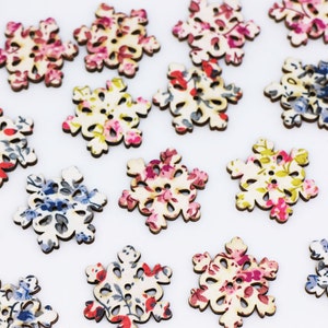 May include: Assortment of wooden snowflake buttons with floral patterns in shades of pink, blue, and green. The buttons are approximately 1 inch in diameter.