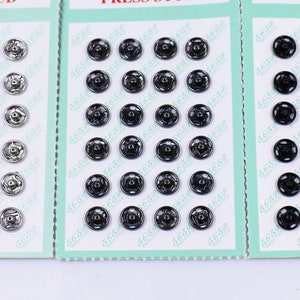 Könnte beinhalten: Drei Karten mit Reihen von silbernen und schwarzen Druckknöpfen. Jede Karte trägt den Text "Press Stud".