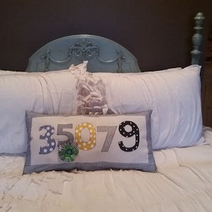 May include: A white bed with a blue headboard and a white pillow with a decorative pillow featuring the numbers 35079 in black, white, and yellow with polka dots.