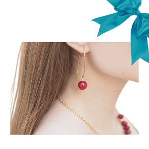 Puede incluir: Aretes de aro de oro con una sola piedra preciosa roja colgando de cada aro.