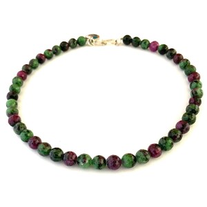 Puede incluir: Un collar de piedras preciosas verdes y rosas con un cierre de plata. El collar está hecho de cuentas redondas.
