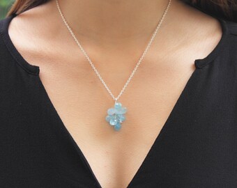 Puede incluir: Un collar de cadena de plata con un racimo de piedras de aguamarina azul claro colgando de él.
