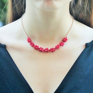 Puede incluir: Un collar de cadena de plata con un racimo de cuentas de piedras preciosas rojas.