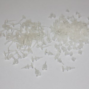 May include: A large pile of clear plastic earring backs. The backs are small and round with a small post sticking out.