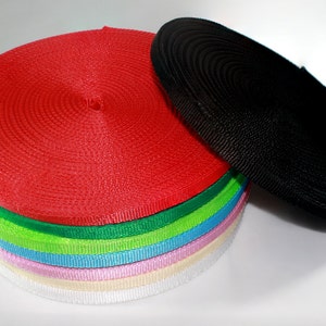 May include: A stack of colorful nylon webbing rolls, including red, green, blue, pink, and white. A black nylon webbing roll is lying on its side next to the stack.