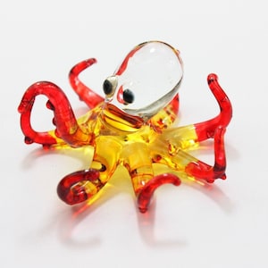 May include: A glass octopus figurine with a clear head and yellow and red body. The octopus has eight tentacles.