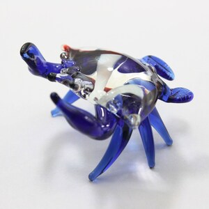 May include: A blue glass crab figurine with white and red accents. The crab has detailed legs and claws.