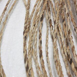 May include: Close-up of a braided cord made from natural fibers. The cord is a light brown color with darker brown accents. It is twisted and woven together to create a strong and durable rope.