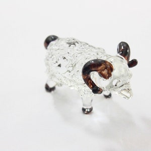 May include: A clear glass figurine of a sheep with brown horns. The sheep is standing on all four legs and has a textured body.