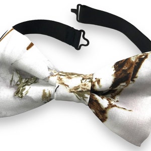 Può includere: Papillon bianco con un motivo floreale marrone e verde. Il papillon ha un cinturino nero regolabile.