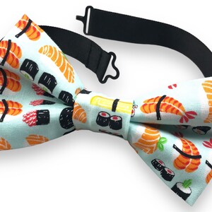 Pode incluir: Uma gravata borboleta azul claro com um padrão de sushi. O padrão inclui vários tipos de sushi, como nigiri, maki e sashimi.