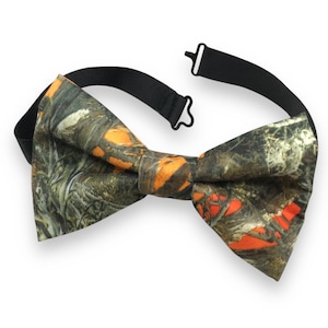 May include: A camouflage bow tie with a black adjustable neck strap. The bow tie features a pattern of green, brown, and orange, resembling a woodland scene. The bow tie is a classic accessory for formal or casual wear.