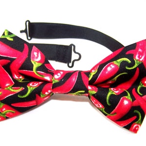 Könnte beinhalten: Eine schwarze Fliege mit einem roten Chili-Muster. Die Fliege hat einen verstellbaren Riemen.