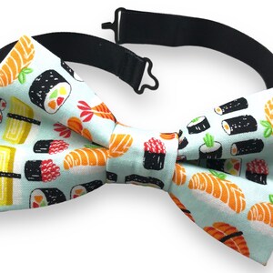 Könnte beinhalten: Ein hellblauer Fliege mit einem Sushi-Druck. Die Fliege zeigt verschiedene Arten von Sushi, darunter Maki-Rollen, Nigiri und Sashimi. Das Sushi ist in Schwarzweiß mit bunten Akzenten gezeichnet.