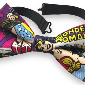 Puede incluir: Una pajarita con estampado de cómic de Wonder Woman. La pajarita es negra y presenta un diseño de cómic rosa, amarillo, azul y rojo con las palabras "Wonder Woman" e "I am Wonder Woman".