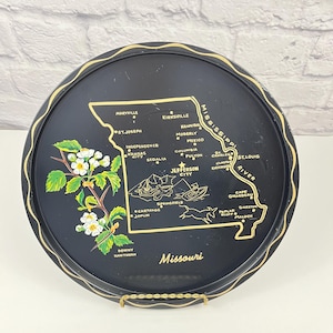 May include: Black round tray with a gold rim and a map of Missouri. The map features cities like St. Louis and Kansas City, with a floral design and the word "Missouri" in white.