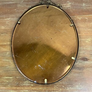May include: The back of an oval-shaped brass picture frame with a decorative design around the edge. The frame is made of a shiny, gold-colored metal.
