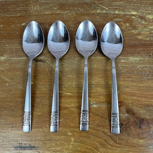May include: Four silver spoons with ornate designs on the handles. The spoons are arranged in a row on a wooden surface.