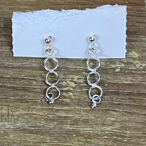 May include: A pair of silver dangle earrings with a chain of four connected circles.