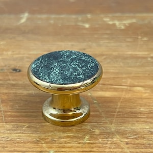 Peut inclure: Un bouton de meuble avec un dessus rond en marbre vert foncé et une base dorée. Le bouton a un design classique et est probablement utilisé pour les meubles ou les armoires. Le dessus en marbre présente un motif naturel unique.