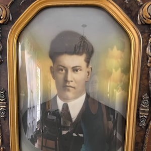 Puede incluir: Un retrato vintage de un hombre con traje oscuro y corbata, enmarcado en un marco ornamentado de color dorado y marrón.