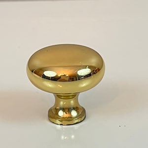 Puede incluir: Un pomo de armario de oro pulido con una parte superior redonda y una base redonda corta.