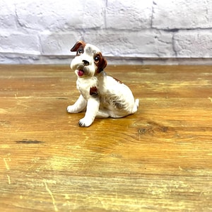 以下が含まれることがあります： 舌を出して座っている犬の白と茶色のセラミック製置物です。
