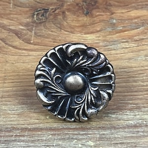 May include: A silver-toned metal cabinet knob with a detailed floral design. The knob has a round shape and a raised center.