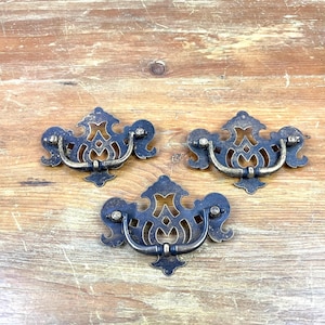 May include: Three ornate, black and gold metal drawer pulls with a decorative, openwork design.