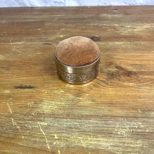 May include: A vintage silver pincushion with an ornate design and a brown velvet top.