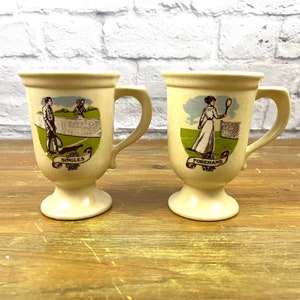 Peut inclure: Deux tasses en céramique crème avec des illustrations sur le thème du tennis. L'une représente un joueur de tennis avec le mot "Singles", l'autre avec "Forehand". Les deux tasses ont une anse et un pied.