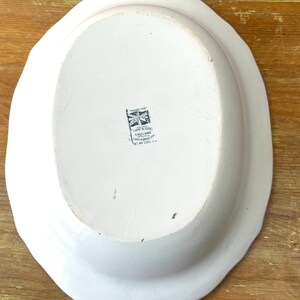May include: White oval serving platter with a scalloped edge. The underside features a black and white emblem with text that reads "IHW & SON ENGLAND". The platter is on a wooden surface.
