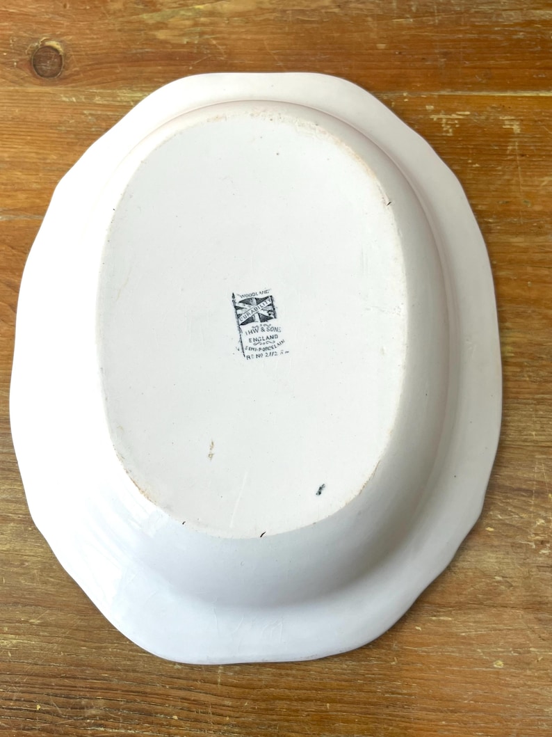 May include: White oval serving platter with a scalloped edge. The underside features a black and white emblem with text that reads "IHW & SON ENGLAND". The platter is on a wooden surface.