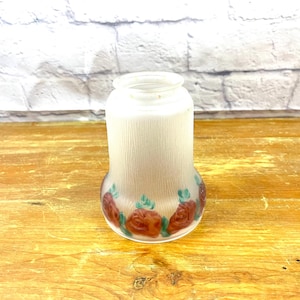 Może przedstawiać: Biały, matowy klosz lampy z wzorem kwiatowym. Klosz ma żebrowaną fakturę i przedstawia czerwone i zielone kwiaty.